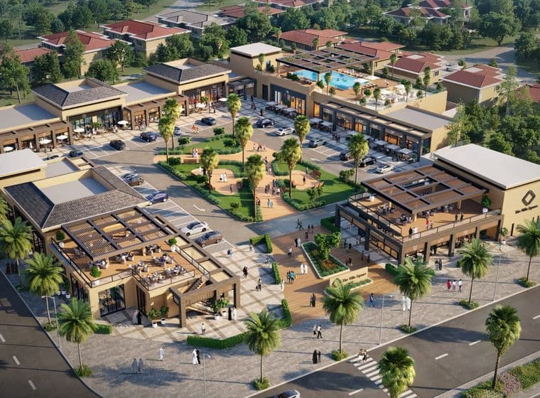 Aerial view of a modern shopping plaza with multiple buildings, outdoor seating, and landscaped areas surrounded by trees and roads.