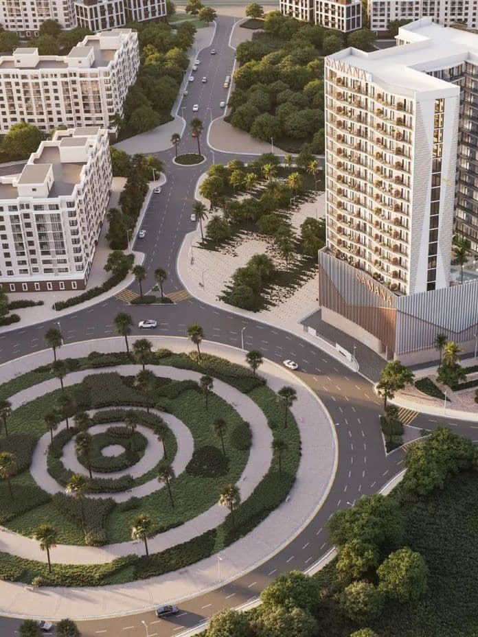 Aerial view of a modern urban area with a tall building marked "Samana," surrounded by roads, smaller buildings, and green spaces.