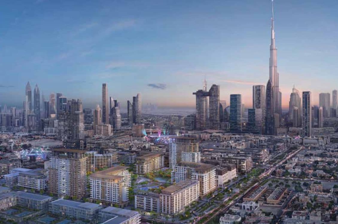 Aerial view of City Walk and Downtown Dubai at dusk, featuring numerous skyscrapers, including a prominent tall tower, under a clear blue sky.