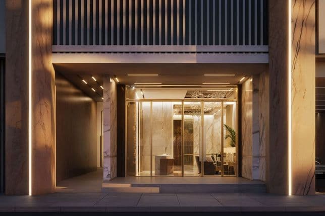 Elegant building entrance with glass doors, warm interior lighting, large marble columns, and modern architectural design.