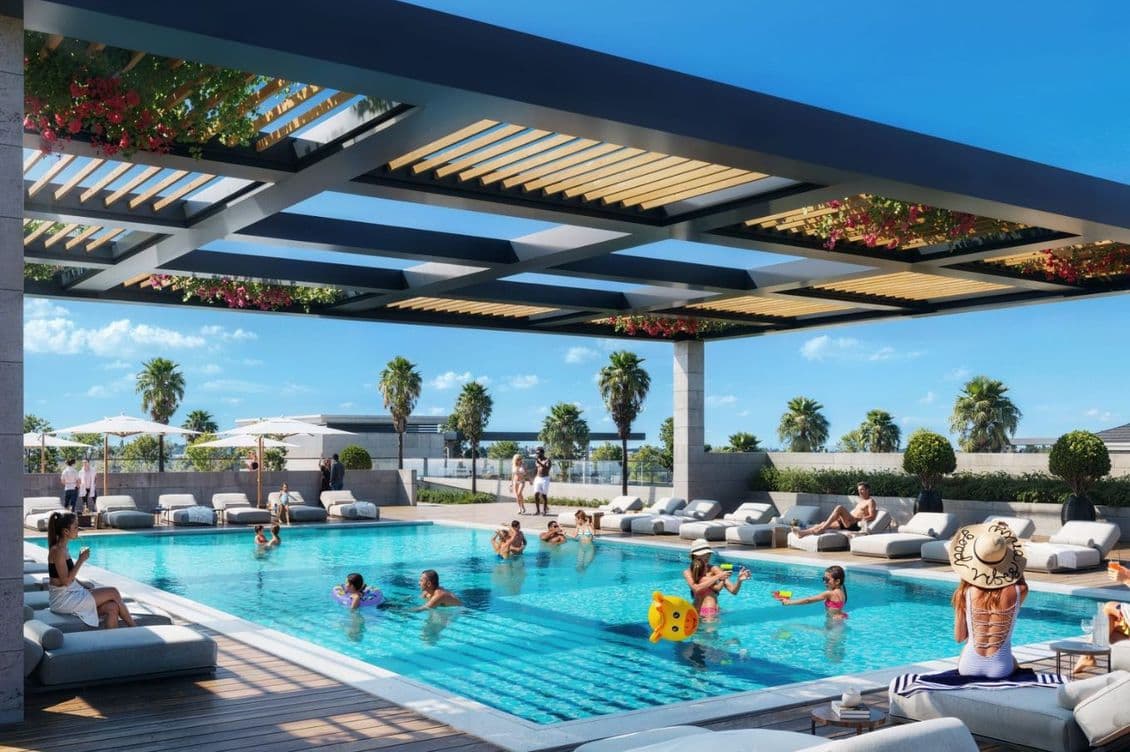 Outdoor pool with people swimming and lounging under a pergola. Palm trees and blue sky in the background.