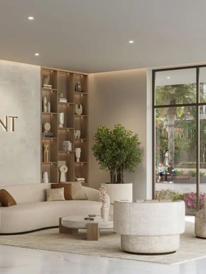 Modern lobby with beige sofas, circular tables, and wall decor. Large window offers view of greenery and pedestrians outside.