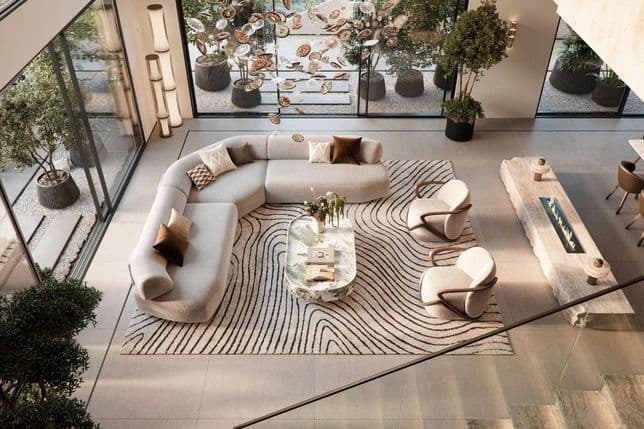 Double-height luxury living room with sculptural chandelier, curved sectional sofa, patterned rug, and full-height glass walls opening to a private garden terrace.