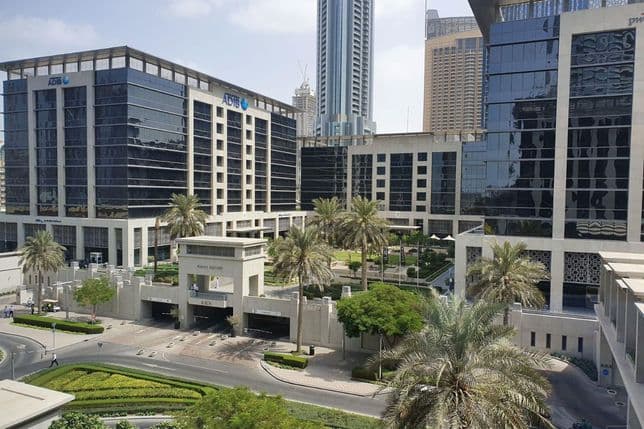 Modern office complex with glass buildings, palm trees, and landscaped greenery under a clear blue sky.