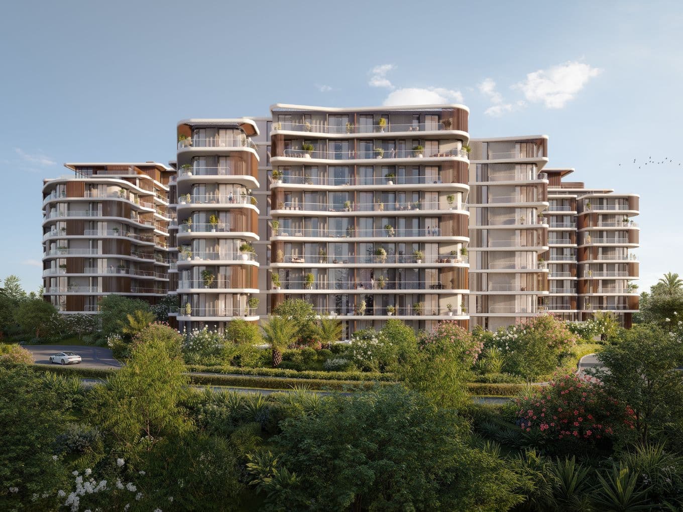 Modern multi-story building with curved balconies, surrounded by lush greenery and a clear blue sky in the background.