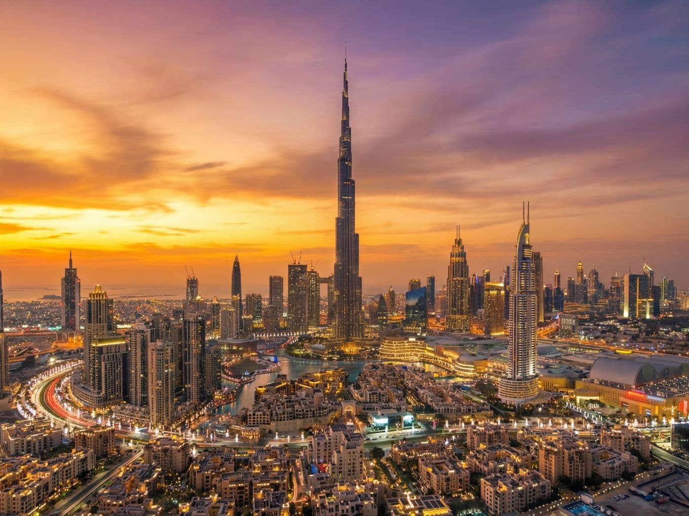 Aerial view of Downtown Dubai at sunset, featuring Burj Khalifa and vibrant orange and purple skies.