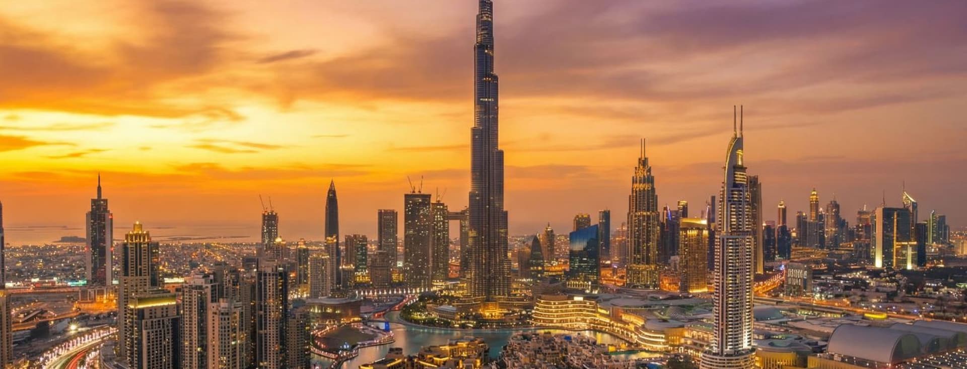 Aerial view of Downtown Dubai at sunset, featuring Burj Khalifa and vibrant orange and purple skies.