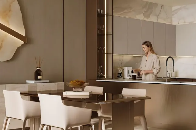 Modern beige kitchen with marble backsplash; a woman stands at the island using a coffee machine while white dining chairs sit around a wooden table. AI-generated image