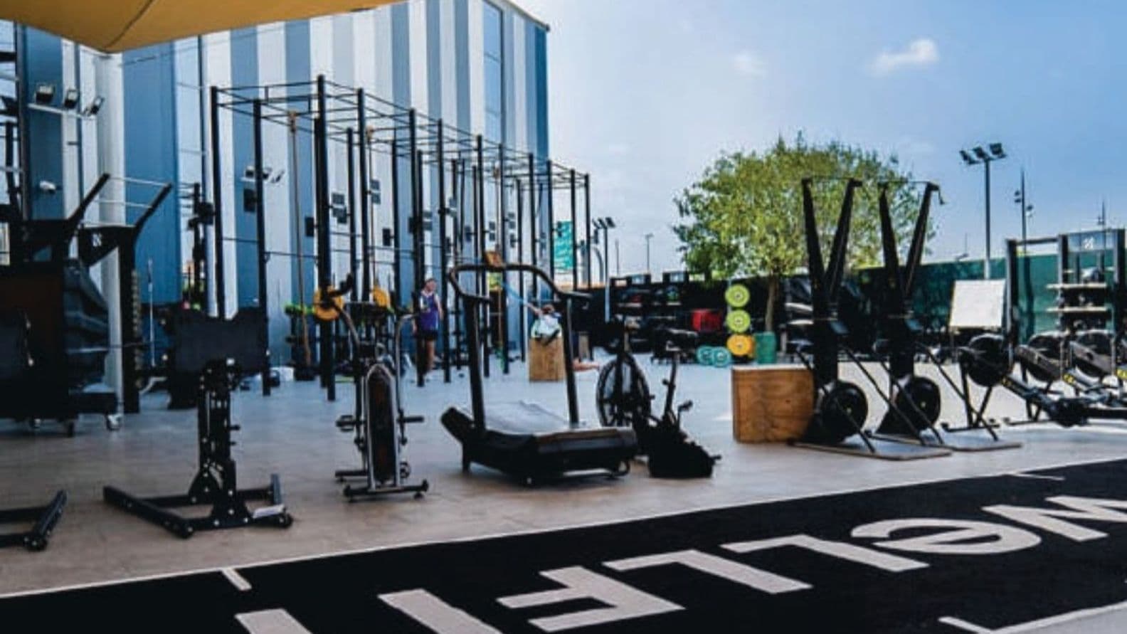 Outdoor gym space with exercise equipment, including stationary bikes and rowing machines, under a yellow canopy.