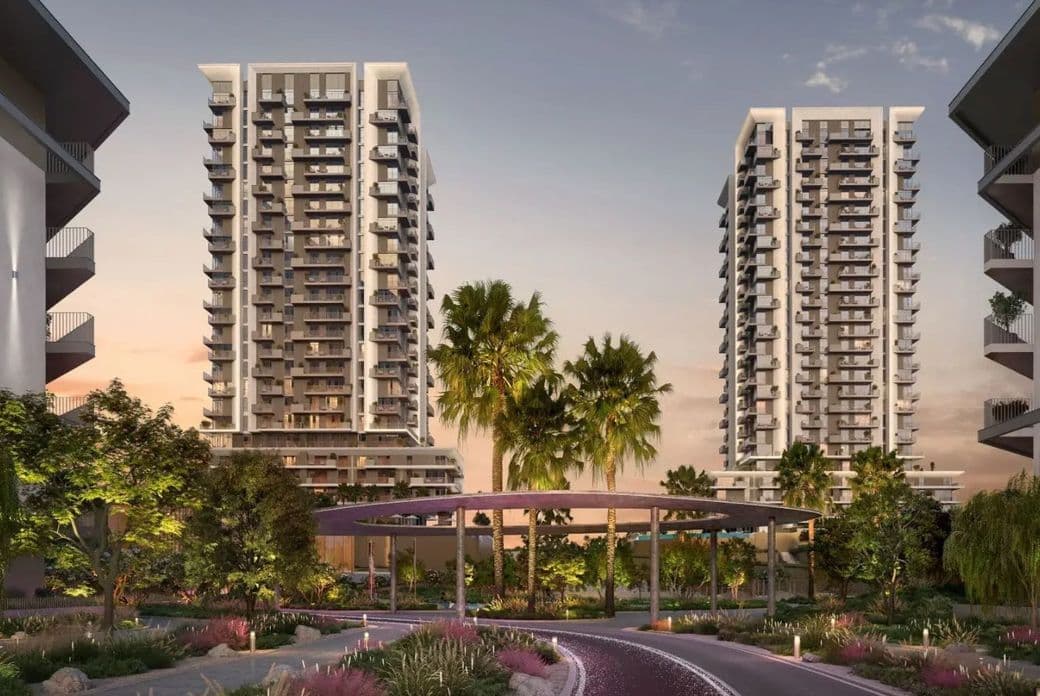 Modern residential towers at Athlon with balconies, surrounded by lush greenery and palm trees, under a twilight sky. Curved pathway in the foreground.