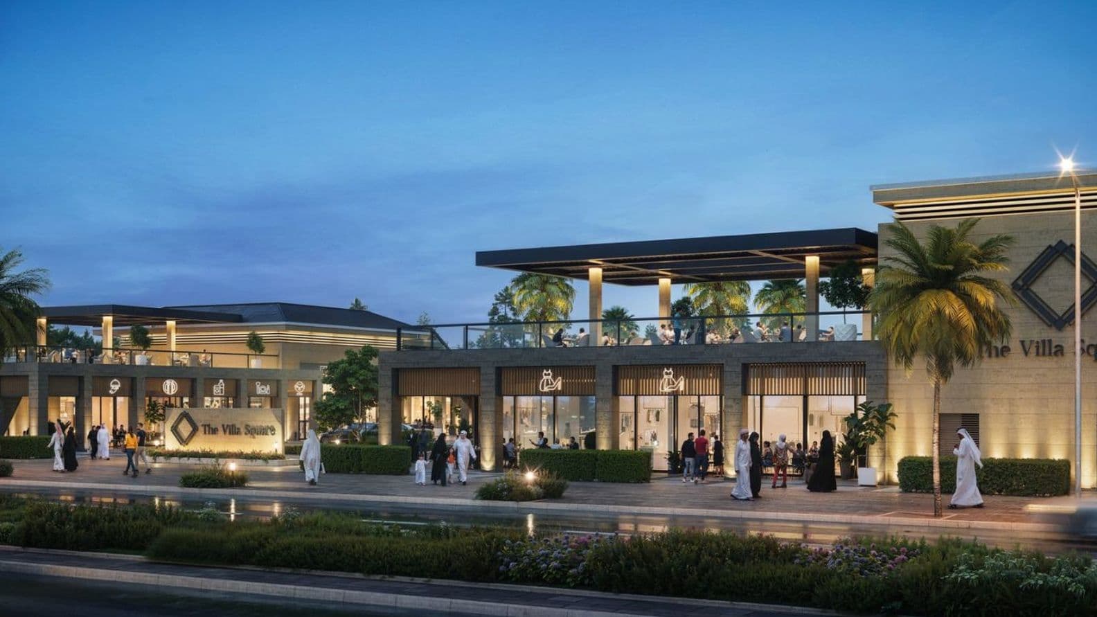 Modern shopping center with palm trees, outdoor seating, and people walking. Illuminated at dusk with a clear sky backdrop.