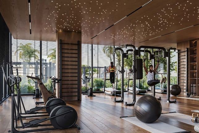 Modern gym with wood floors, starry ceiling, and large windows. Equipment includes bikes, a punching bag, and an exercise ball. People working out.
