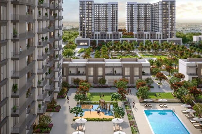 Modern apartment complex with tall buildings, greenery, a playground, and a swimming pool surrounded by lounge chairs and umbrellas.