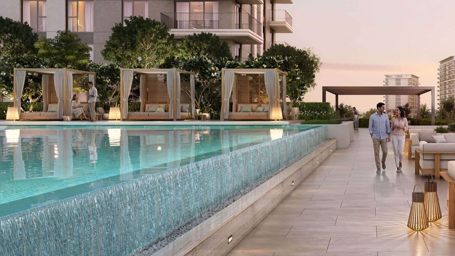 Modern rooftop pool with cascading edge, cabanas and lit lanterns, couple walking along tiled deck beside high-rise apartments at dusk
