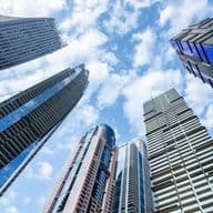 Upward view of modern skyscrapers with various designs against a blue sky dotted with clouds, creating a dramatic urban skyline.