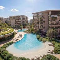 Modern apartment complex with lagoon-style pool, sandy beach edge, lounge chairs and lush landscaping