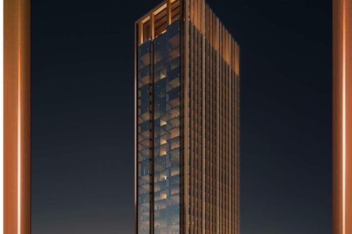 Tall, modern skyscraper with glass facade and warm lighting, set against a dark night sky between two vertical orange pillars.