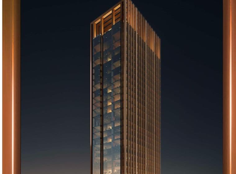 Hoher, moderner Wolkenkratzer mit Glasfassade und warmer Beleuchtung, vor dem Hintergrund eines dunklen Nachthimmels zwischen zwei vertikalen orangefarbenen Säulen.