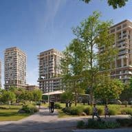 People strolling in a green park with pathways and trees, foregrounding modern high-rise apartment towers under a clear blue sky.
