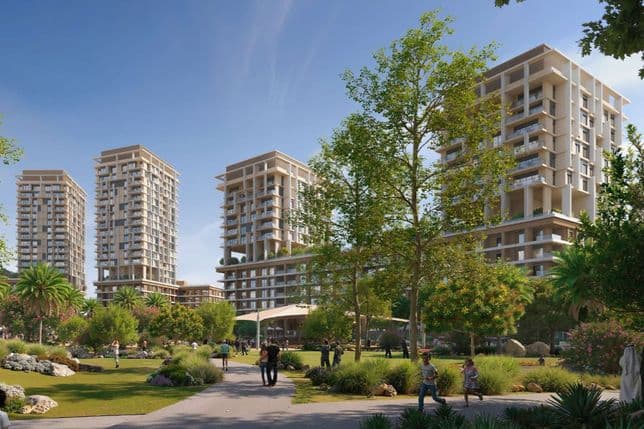 People strolling in a green park with pathways and trees, foregrounding modern high-rise apartment towers under a clear blue sky.