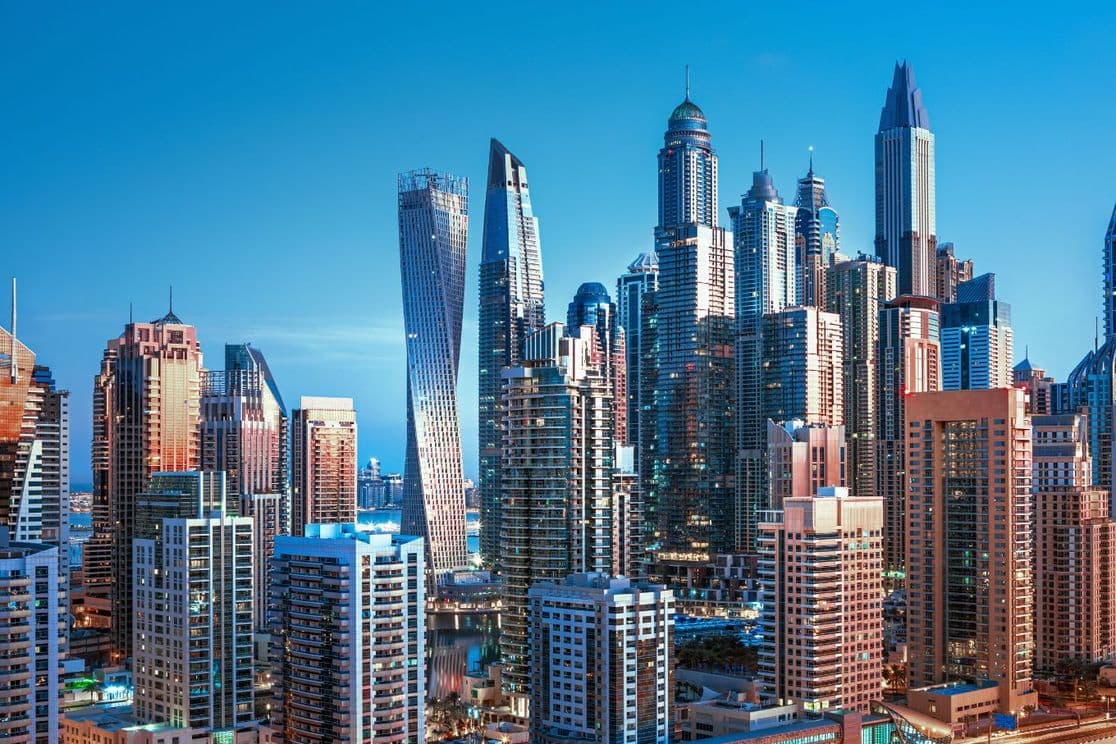 Evening cityscape of Dubai Marina highlighting Cayan Tower and illuminated skyscrapers against a deep blue sky.