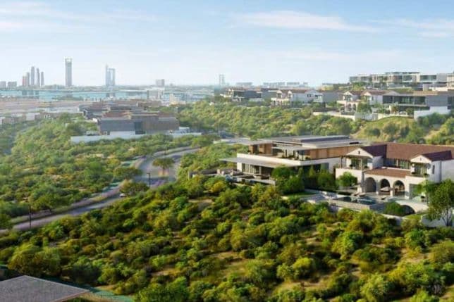 Hilly landscape with modern villas surrounded by greenery. Skyscrapers are visible in the distant skyline under a clear blue sky.
