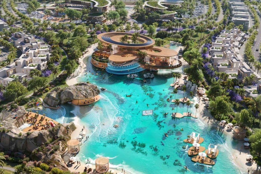 Aerial view of a luxury resort with villas, a turquoise pool, palm trees, and various recreational areas, surrounded by greenery and parking.