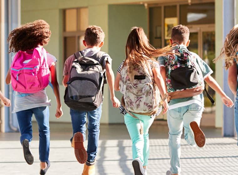 A group of school children with backpacks joyfully running.