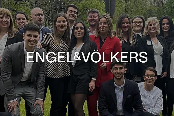 Un groupe d'agents immobiliers Engel & Völkers posent en extérieur, souriant à la caméra. Les agents portent des tenues professionnelles en noir, rouge et gris.