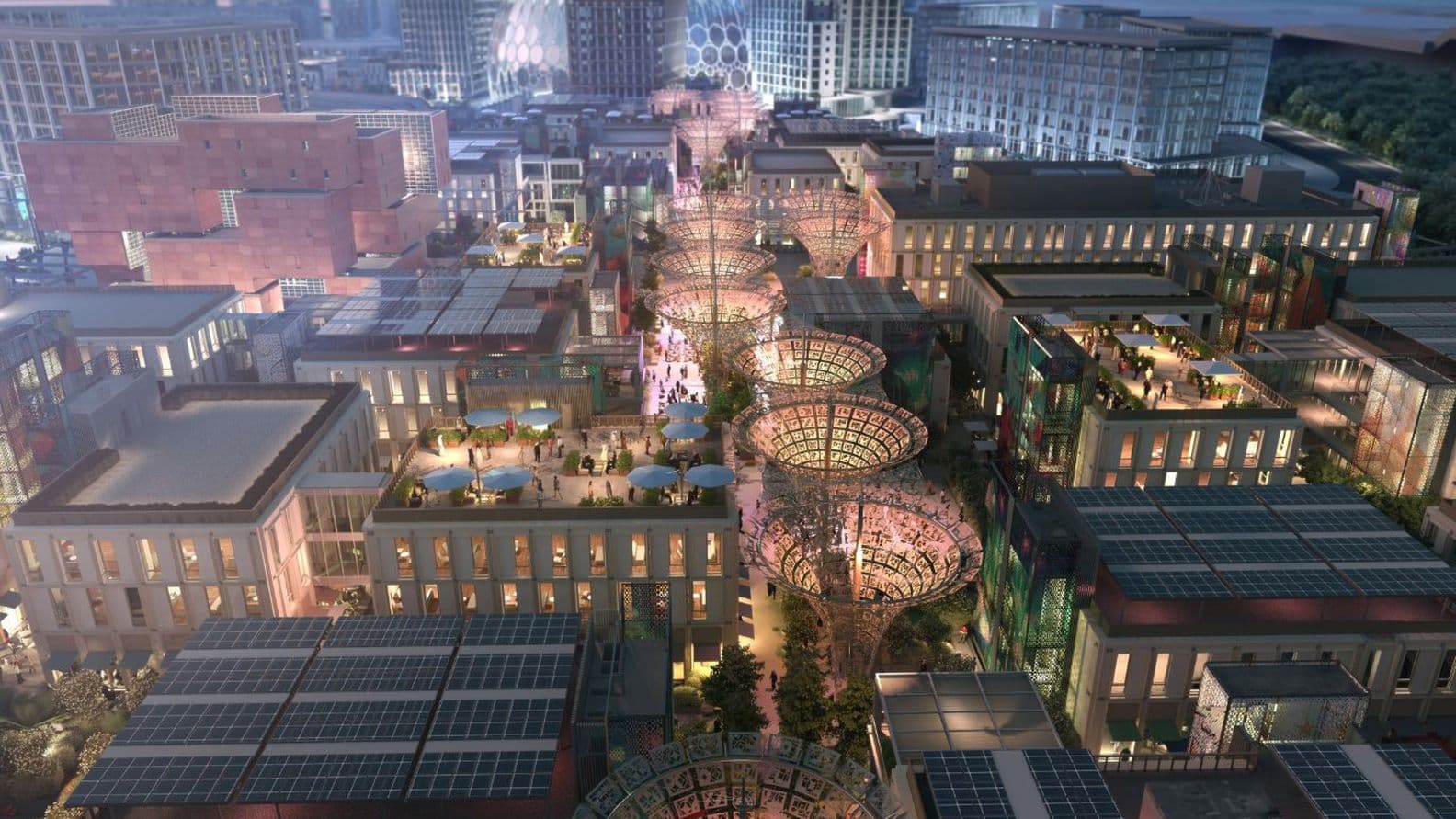 erial night view of Expo City Dubai showcasing tree-shaped solar canopies, rooftop terraces, landscaped courtyards, and the illuminated Al Wasl Dome in the background.
