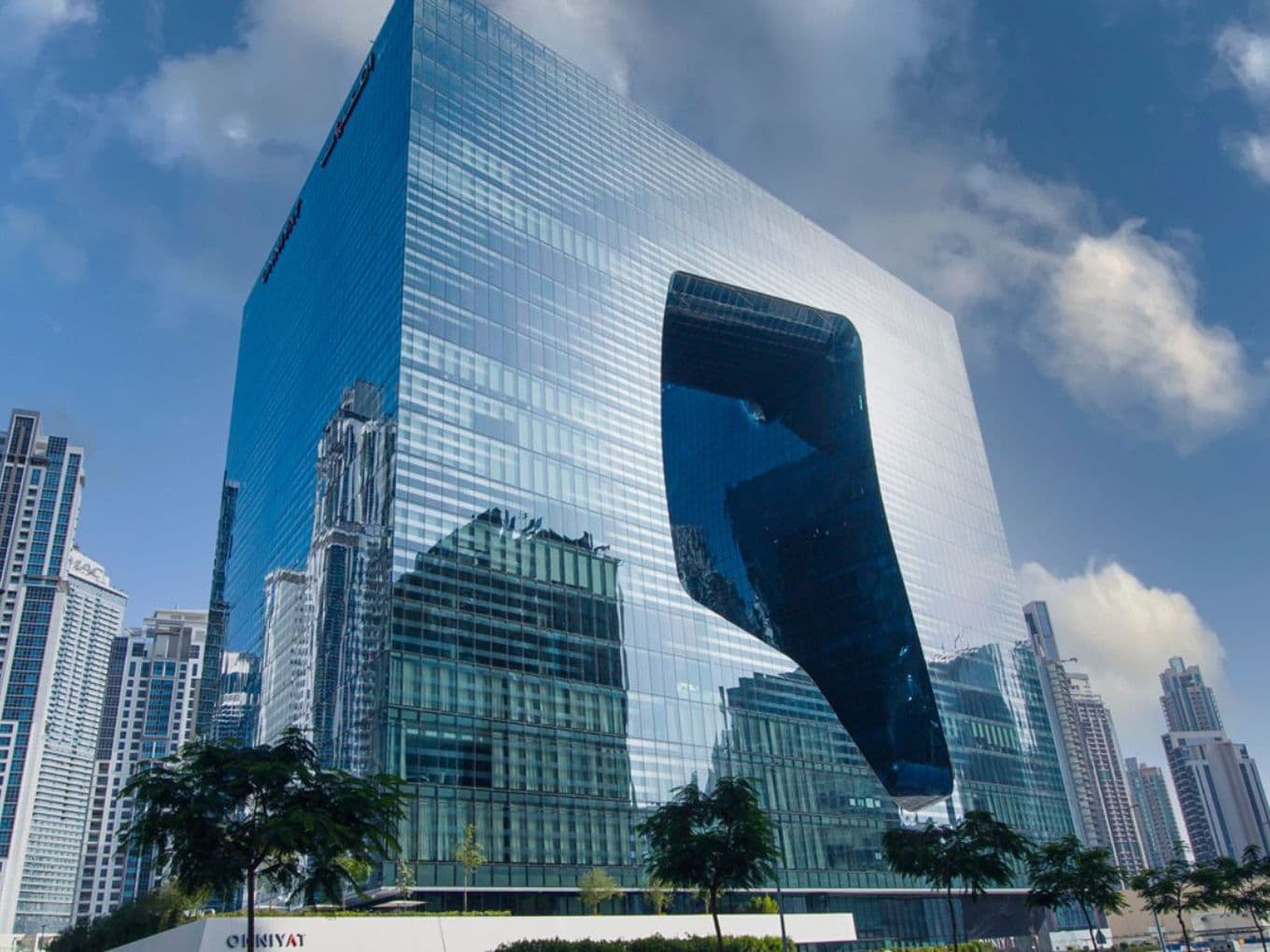 Reflective glass façade of The Opus tower showcasing its unique sculptural design with curved cut-out void.