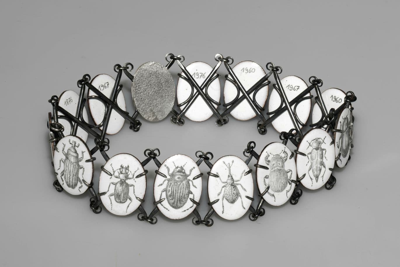 Ein Choker mit Emailleplatten, auf denen handgezeichnete Käfer und die Jahreszahlen 1960 bis 1967 eingraviert sind.
