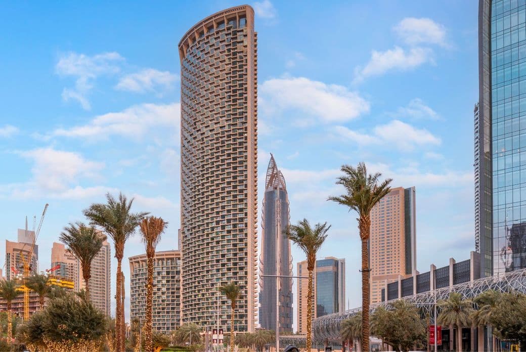 Hoher, geschwungener Burj Vista Tower in Dubai, umgeben von mit dekorativen Lichtern umwickelten Palmen, modernen Wolkenkratzern und einem blauen Himmel mit vereinzelten Wolken.
