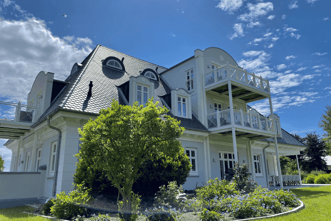 Large villa with a green tree in the foreground under a bright blue sky
