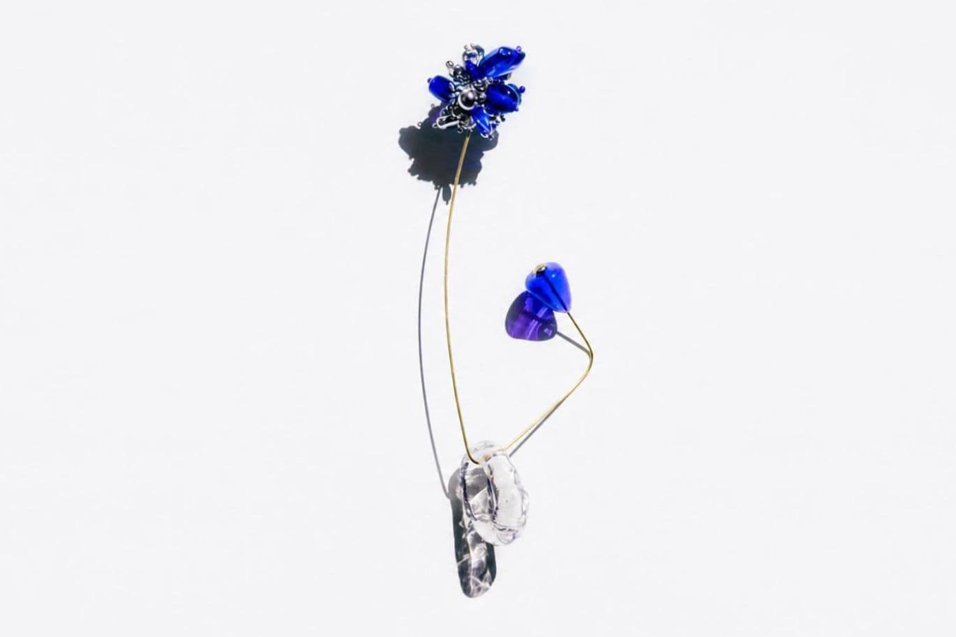 Drahtperlen-Skulptur: oben eine hohe blaue Glasblume, goldene Drähte mit violetten und klaren Perlen vor weißem Hintergrund.