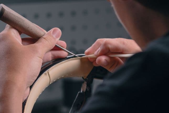 Eine Person, die mit Nadel und Faden Leder auf ein Lenkrad näht. Ihre Hände sind konzentriert und detailorientiert.
