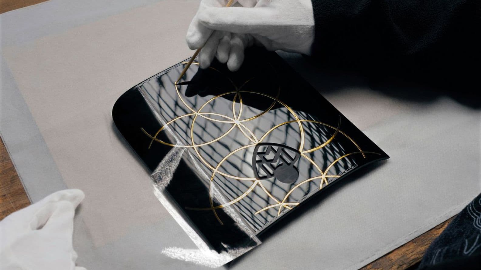 Hände in weißen Handschuhen malen komplizierte goldene Muster auf eine glänzende schwarze, gewölbte Oberfläche.