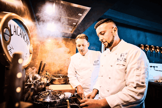 zwei Köche am Lacanche Herd, beide auf Topf schauend