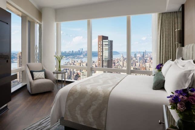Bright bedroom with floor-to-ceiling windows and sweeping views of the New York skyline and Hudson River.