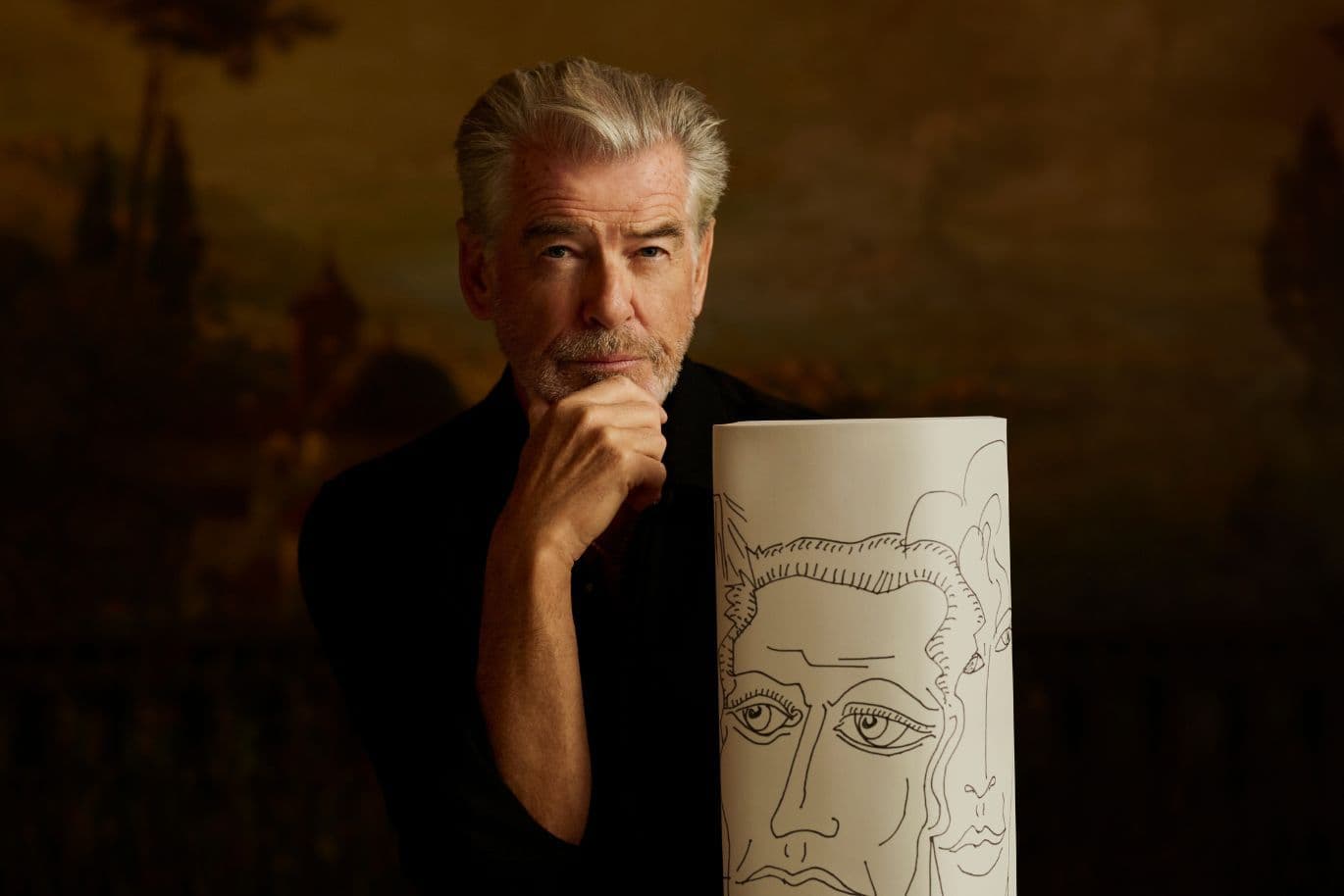 Mann mit grauen Haaren und nachdenklichem Gesichtsausdruck lehnt an einem Zylinder mit abstrakten Gesichtszeichnungen, dunkler und künstlerischer Hintergrund.