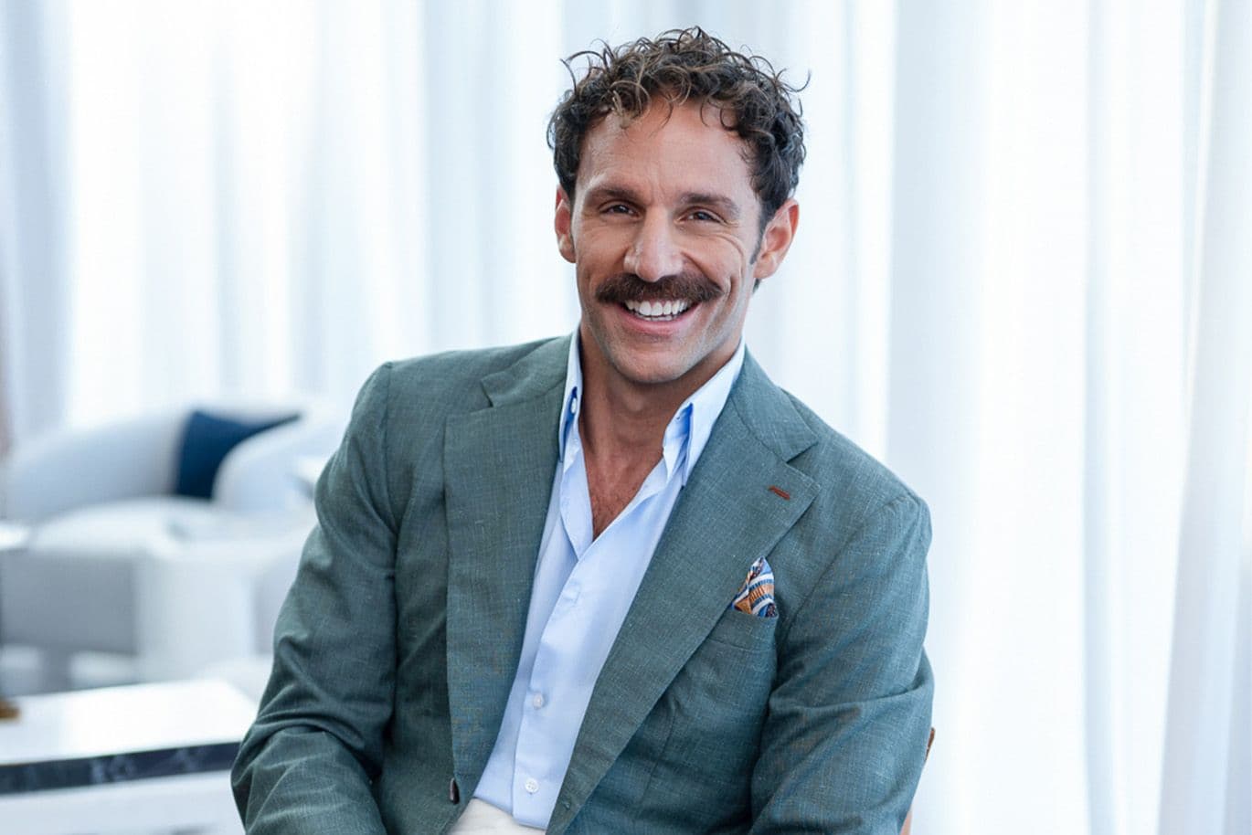 Άνδρας με κοστούμι, κάθεται σε μια καρέκλα και χαμογελά