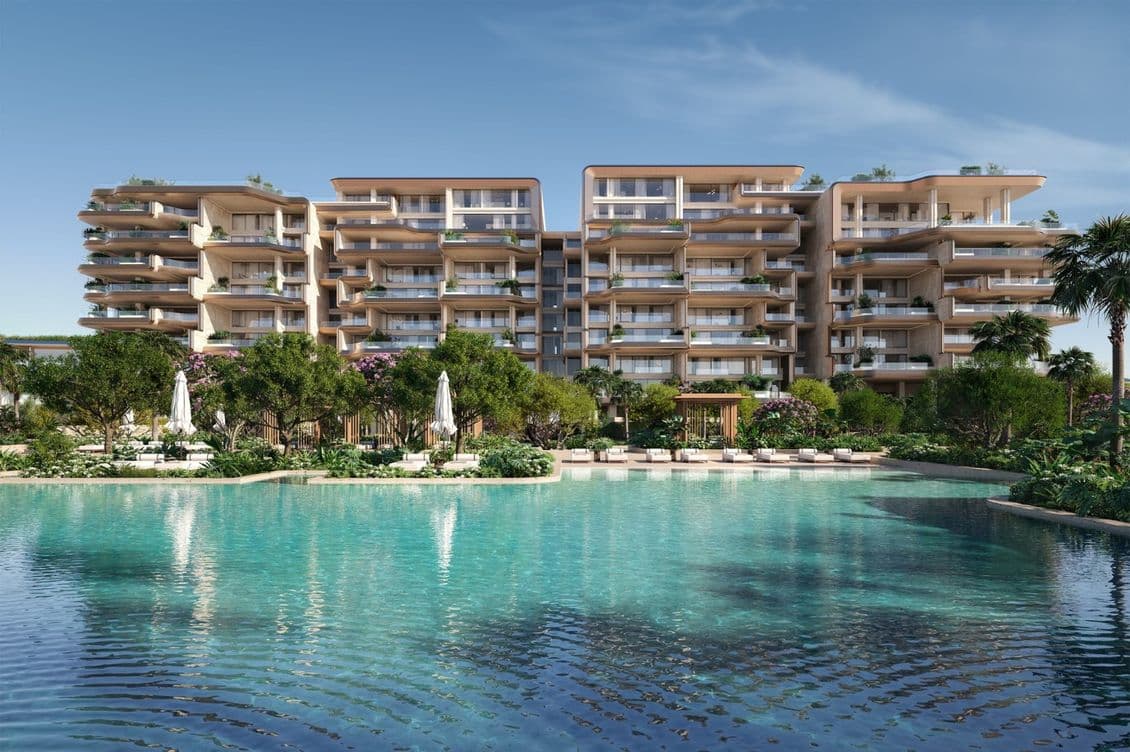 Luxurious beachfront apartments by luxury developer Omniyat with modern architecture, surrounded by lush greenery and a large, inviting swimming pool under a clear blue sky.