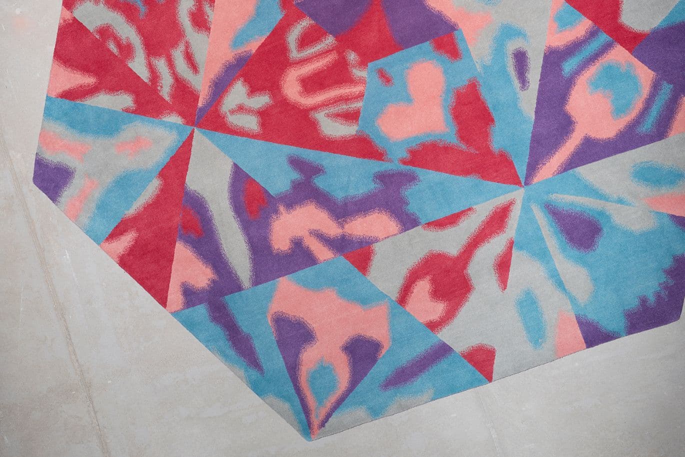 Farbenfroher geometrischer Teppich mit abstrakten Kaleidoskopmustern in Rot, Blau, Violett und Rosa auf hellbeigem Boden.