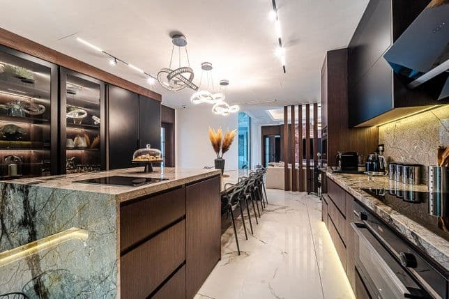Modern kitchen with marble countertops, dark wood cabinetry, stylish lighting, and a dining area with a long table and chairs.