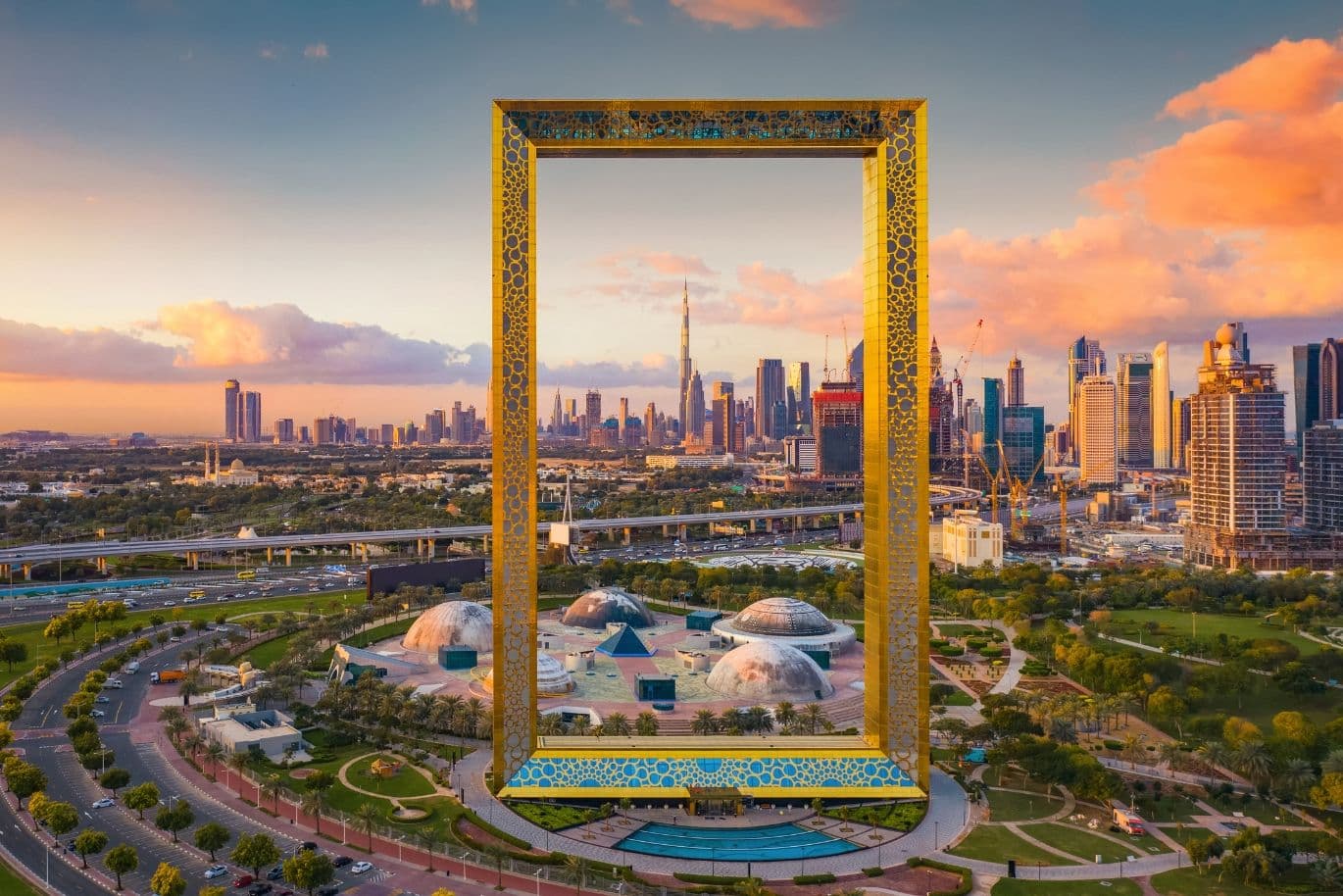 Aerial view of the Dubai Frame at sunset, with the city skyline in the background, including the Burj Khalifa.
