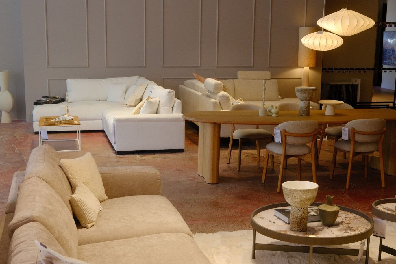 A modern living room with beige and white sofas, a wooden dining table, chairs, and decorative lighting in a cozy, elegant setting.