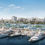 Luxury yachts docked in the marina at Mina Rashid, Dubai, with modern mid-rise waterfront residences, palm-lined promenades, and the city skyline, including Burj Khalifa, visible in the background under a clear blue sky.          Ask ChatGPT