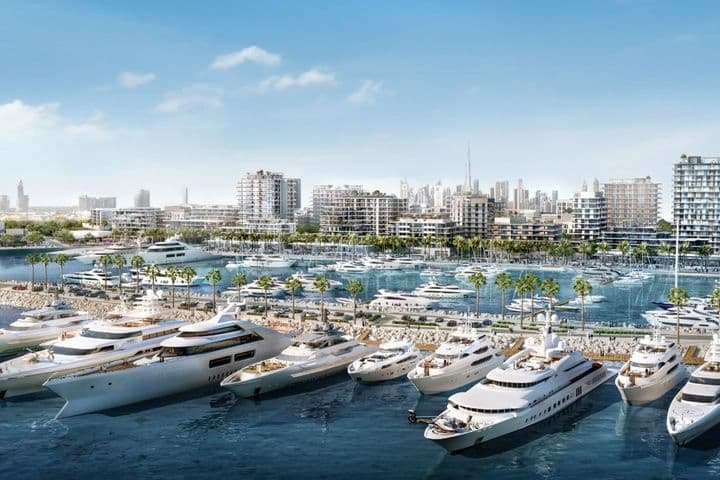 Luxury yachts docked in Rashid Yachts and Marina, with modern mid-rise waterfront residences, palm-lined promenades, and the city skyline, including Burj Khalifa, visible in the background under a clear blue sky.          Ask ChatGPT