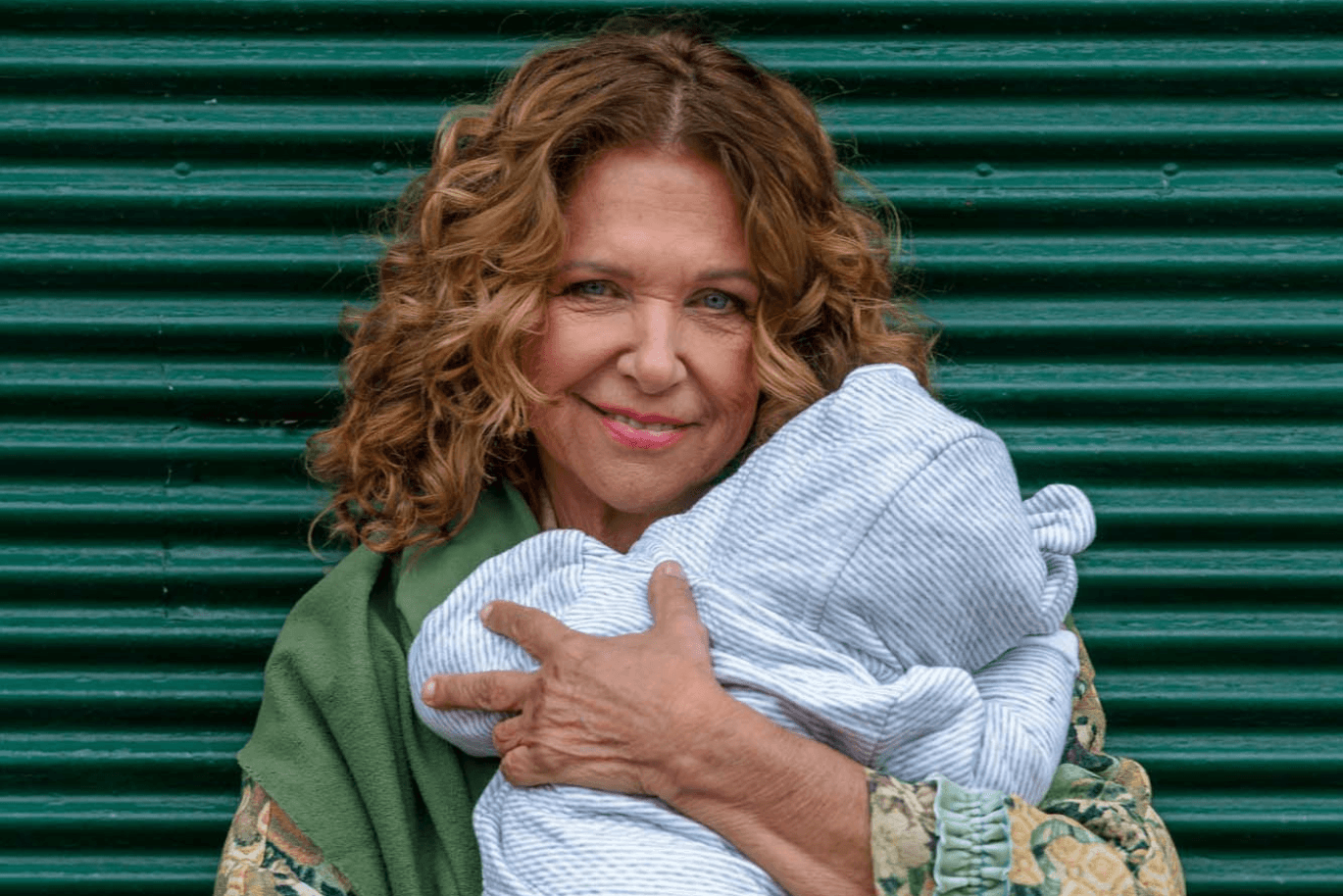 Haya Molcho smiling while holding a baby in her arms.
