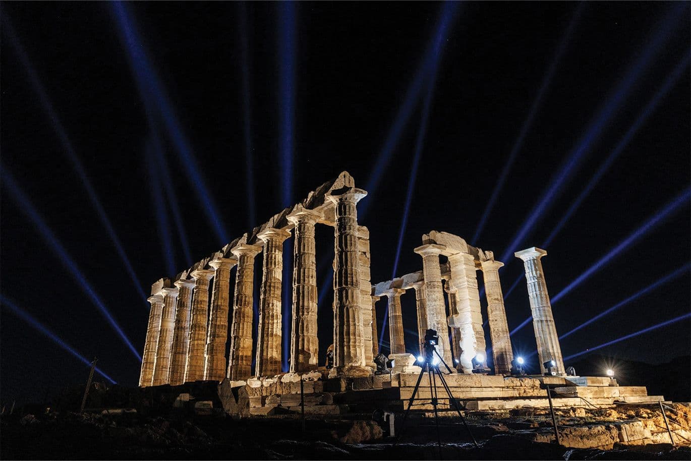 Ο Ναός του Ποσειδώνα στο Σούνιο φωτισμένος εντυπωσιακά με δέσμες φωτός που διαχέονται στον νυχτερινό ουρανό.